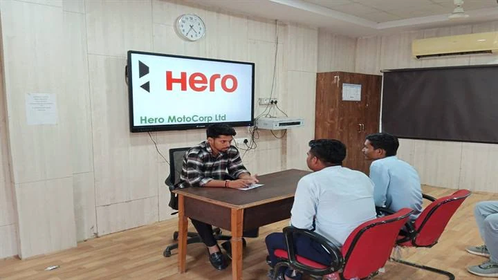 हीरो मोटोकॉर्प के स्क्रीन वाले कक्ष में मेज पर बैठकर साक्षात्कार देते अभ्यर्थी